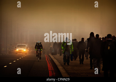 Un ciclista mascherato e pendolari che viaggiano attraverso il London Bridge su una mattina smoggy Foto Stock