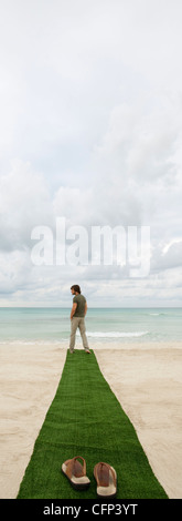 Uomo in piedi alla fine del tappetino sulla spiaggia, sandali in primo piano Foto Stock