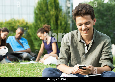 Giovane uomo per la messaggistica di testo con un telefono cellulare, un gruppo di persone in background Foto Stock