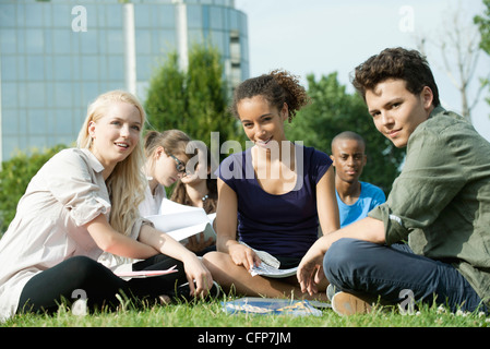 Gli studenti universitari che studiano insieme all'aperto su erba, concentrarsi su una sola donna Foto Stock