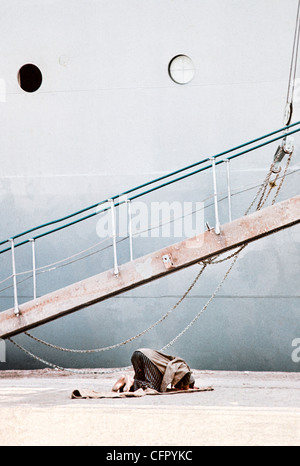 IRAN, BANDAR SHAHPUR: musulmana lavoratore dock si inginocchia a pregare verso la Mecca accanto a una nave cargo schierate per caricare il carico. Archival Foto Stock