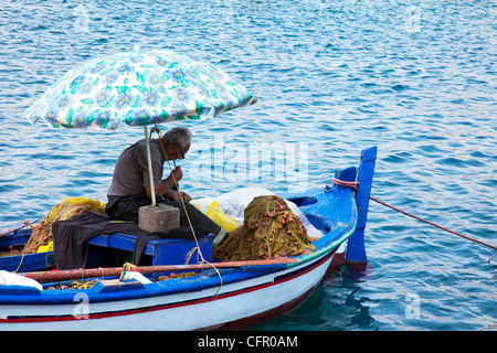Tipico vecchio pescatore greco partecipando alle sue reti da pesca mentre ancora sulla sua barca per i prossimi giorni viaggio a Cefalonia Foto Stock