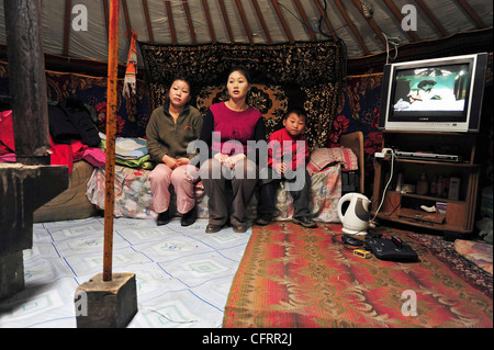 Mongolia, Baganuur, famiglia in abbigliamento casual, seduto sul divano in yurta dalla televisione e guardando lontano Foto Stock