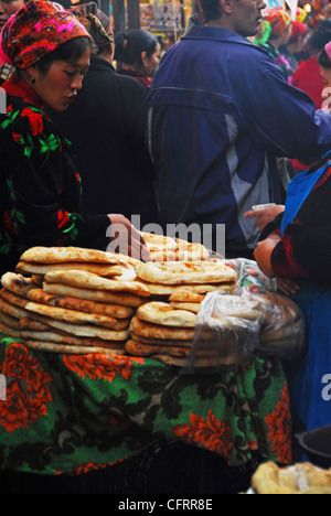 Uzbekistan, Urgut, vista della donna acquistare panini visualizzati in stallo con persone camminare in background Foto Stock