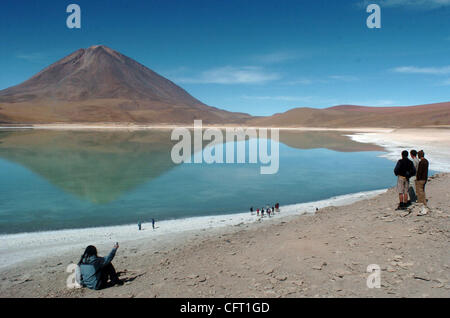 Dic 04, 2006 - Uyuni, Bolivia - un 'gringo' (straniero), sinistra lontana, prende una foto di "Laguna Verde" (verde Laguna) con il suo telefono cellulare mentre è seduto sulla laguna della banca. Il Salt Lake prende il colore distinto da sedimenti con i minerali di rame e si trova sul confine cileno ai piedi del vo Foto Stock