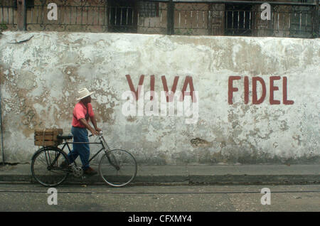 Apr 20, 2007 - Santiago de Cuba, Cuba - un uomo cubano trasporta la frutta fresca da un mercato locale in bicicletta di fronte le parole 'Viva Fidel' (Evviva Fidel!) dipinta su una casa della parete esterna in una zona residenziale della città orientale. La Propaganda come questo, anche fatto semplicemente con la vernice, è trovato thr Foto Stock