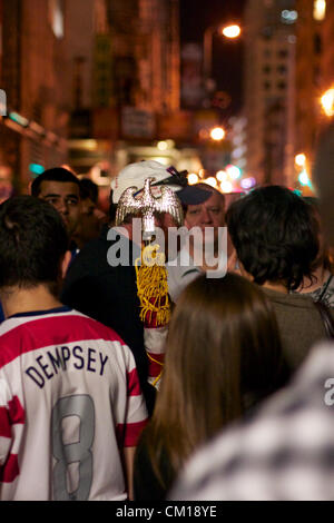 New York, NY - Settembre 11, 2012: un uomo in uniforme FDNY detiene una bandiera americana e i colloqui per una folla in un memoriale vicino al World Trade Center sito in costruzione come è acceso in rosso, bianco e blu nella memoria del 9/11 attacchi 11 anni prima. Foto Stock