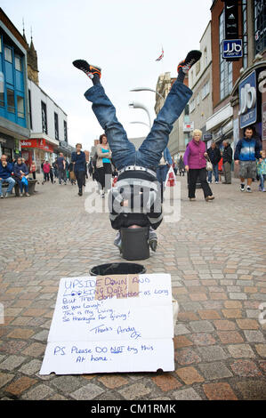 Blackpool, Regno Unito. Sabato 15 settembre 2012. Blackpool l uomo viene capovolta economia a suo vantaggio. 'Capovolto Andy' vivendo in piedi a testa in giù con la sua testa in una benna per il divertimento degli acquirenti in Blackpool Town Center. Foto Stock