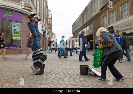 Blackpool, Regno Unito. Sabato 15 settembre 2012. Blackpool l uomo viene capovolta economia a suo vantaggio. 'Capovolto Andy' vivendo in piedi a testa in giù con la sua testa in una benna per il divertimento degli acquirenti in Blackpool Town Center. Foto Stock