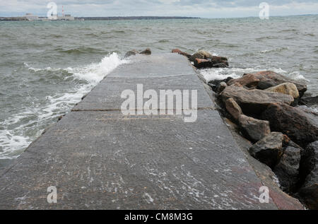 Niantic, East Lyme, Connecticut USA 28 Ott 2012 Il giorno prima di uragano di sabbia costiera ha colpito New England, venti, whitecaps e surf pesante costruire lungo la riva del Connecticut. Onde che si infrangono spazzolata attraverso un molo sulla spiaggia principale ai piedi della strada Whitecap in spiaggia comunità del punto di nero. La macina del mulino centrale nucleare è visto attraverso la baia. Foto Stock