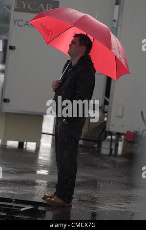 Xx Luglio 2012, Silverstone, Regno Unito un uomo ripara dalla pioggia sotto un ombrello rosso come la pioggia cade a Silverstone Classic 2012 Foto Stock