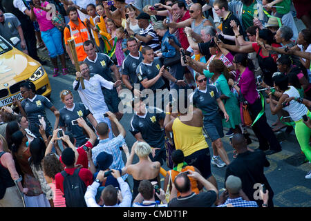 La Torcia olimpica arriva giù Coldharbor Lane in Brixton, Londra, Regno Unito. I torchbearer è protetto dalla polizia in grigio sportswear e il relè è preceduta da sponsor veicoli. Il 26 luglio 2012. Foto Stock