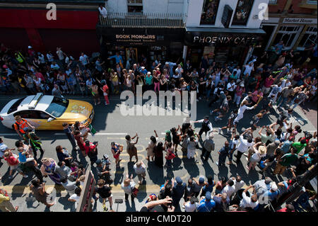 La Torcia olimpica arriva giù Coldharbor Lane in Brixton, Londra, Regno Unito. I torchbearer è protetto dalla polizia in grigio sportswear e il relè è preceduta da sponsor veicoli. Il 26 luglio 2012. Foto Stock