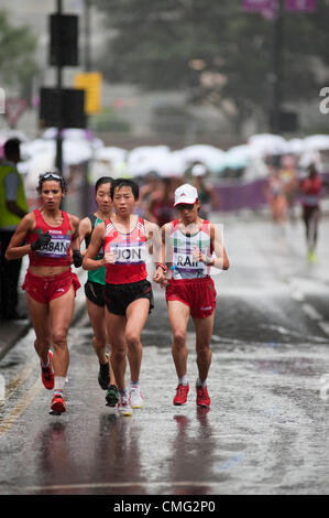 I Giochi Olimpici di Londra 2012 Womens corridori della maratona approccio la City di Londra dal terrapieno in piogge torrenziali a 24 minuti nella corsa su strada. Linea di spettatori il percorso il ricovero sotto gli ombrelloni Foto Stock