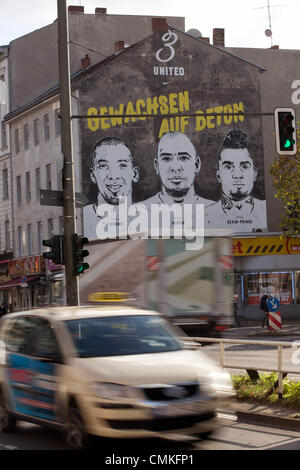 Berlin-Wedding, Germania. 30 ott 2013. Un sporting buon costruttore pubblicizza con le facce dei fratelli Girolamo (L-R), George e Kevin-Prince Boateng su una parete di un edificio in Berlin-Wedding, Germania, 30 ottobre 2013. Schalke's pro soccer player Kevin-Prince Boateng avrebbe imparato a giocare a calcio in questa gabbia. Foto: Joerg Carstensen/dpa/Alamy Live News Foto Stock