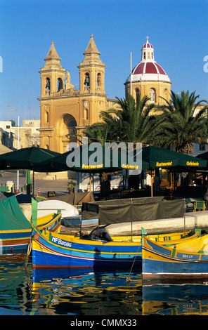 Porto con Luzzu barche da pesca e Marsaxlokk Chiesa Parrocchiale, Marsaxlokk, Malta, Mediterraneo, Europa Foto Stock