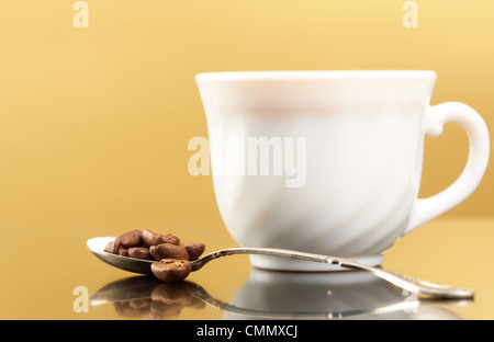 Foto della tazza in porcellana con cucchiaio pieno di chicchi di caffè nelle vicinanze Foto Stock