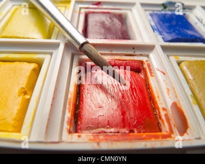 Primo piano della spazzola in bilico sopra compressa di rosso il colore dell'acqua in una scatola di vernice. Foto Stock