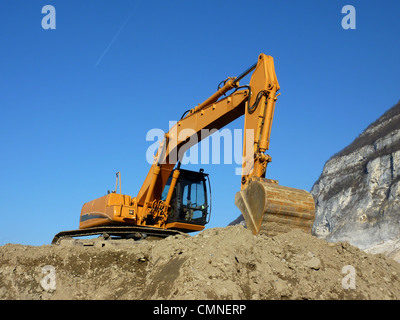 Grande escavatore arancione in piedi sul suolo in prossimità di una montagna Foto Stock