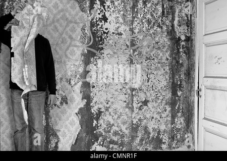 La figura oscurate con carta da parati strappata in abbandonato interni. In bianco e nero. Foto Stock