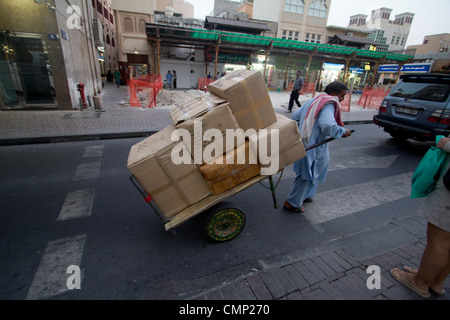 Emirati Arabi Uniti, Dubai - Un uomo tira un carrello carico di scatole di cartone attraverso una strada di mercato a Bur Dubai, consegnando merci in uno dei quartieri commerciali storici della città Foto Stock
