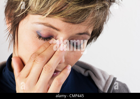 Triste giovane donna tenendo la mano al suo volto - ritratto femminile con gli occhi chiusi. Studio shot contro uno sfondo bianco. Foto Stock