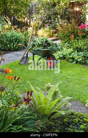 Sera dopo il lavoro nel giardino estivo con carriola, pala e rastrello - verticale Foto Stock