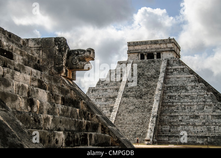 Piattaforma El Castillo Venere Chichen Itza Yucatan Messico | CHICHEN ITZA, Messico - Una testa di serpente intagliata fissa la balaustra della piattaforma Venere in primo piano, con El Castillo che sorge dietro di essa attraverso la piazza. La piattaforma prende il nome dal pianeta Venere, il cui ciclo sinodico gli astronomi Maya tracciarono con precisione e codificarono nell'architettura cerimoniale del gruppo settentrionale di Chichen Itza. El Castillo si erge a circa 98 piedi (30 m) su nove terrazze. Foto Stock