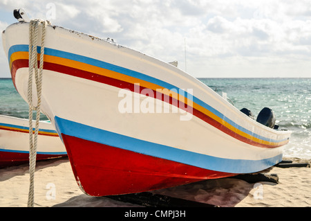 Barca da pesca sulla spiaggia di Playa del Carmen Messico | PLAYA DEL CARMEN, Quintana Roo, Messico — Due barche da pesca a strisce abbinate sono tirate sulla sabbia, le loro prue rivolte verso il Mar dei Caraibi sotto un cielo nebbioso. Le barche costruite e dipinte come questi skiff panga hanno a lungo servito la piccola pesca che ha preceduto la crescita di Playa del Carmen in una grande città turistica. Gli scafi in legno e i motori fuoribordo gemelli sono tipici delle imbarcazioni costiere utilizzate in tutta la penisola dello Yucatán. Foto Stock