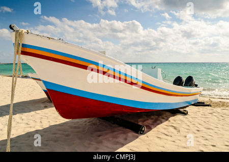 Un dipinto luminosamente barca tirata sulla sabbiosa spiaggia di Playa del Carmen sulla penisola dello Yucatan in Messico con poco nuvoloso sky in background. Foto Stock