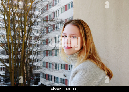 Una giovane ragazza si erge sul balcone di un appartamento house city e guarda nella telecamera Foto Stock