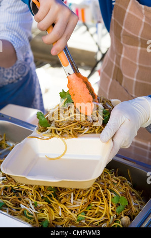 Tagliatelle di essere servito in una vaschetta di polistirolo da una persona che indossa guanti di gomma mediante alette servente Foto Stock