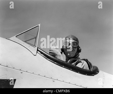 1940s sorridente esercito aria CORPS pilota nel pozzetto aperto indossando un cuoio battenti casco dando un pollice in alto segno Foto Stock