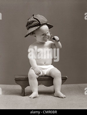 1940s BABY Sherlock Holmes nel pannolino seduta sul banco indossando DEER STALKER HAT guardando attraverso la lente di ingrandimento Foto Stock