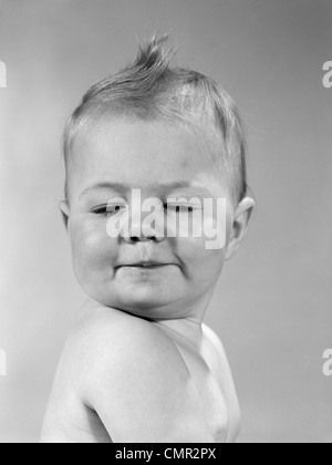 Anni sessanta VISTA LATERALE DEL BAMBINO ritratto con il mento sulla spalla e gli occhi chiusi SMIRKING girando la testa verso la telecamera Foto Stock