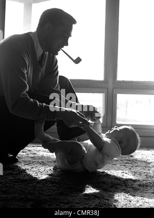 Degli anni Cinquanta padre TUBO IN BOCCA in ginocchio per giocare con il bambino posa sul pavimento la luce del sole proveniente da Windows Foto Stock