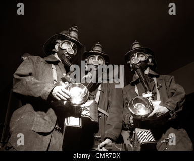 Anni Cinquanta il trio della squadra di salvataggio per i vigili del fuoco di indossare il respiratore maschere portando torce E ATTREZZATURA ANTINCENDIO Foto Stock