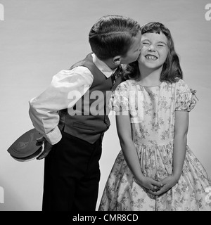 Anni Cinquanta anni sessanta BOY IN VEST & bow tie HOLDING VALENTINE CANDY baciando la guancia della ragazza FACENDO UNA FACCIA Foto Stock
