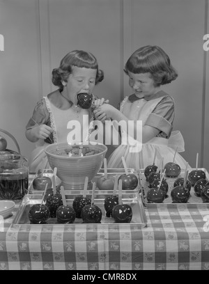 Anni Cinquanta due figlie gemelle di mangiare facendo CANDY LE MELE IN CUCINA Foto Stock