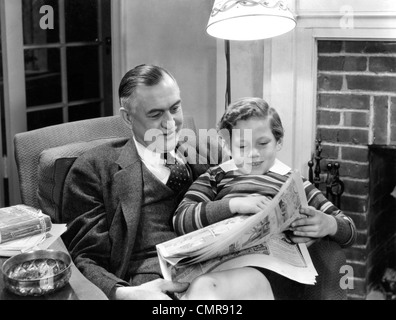 1930s 1940 nonno seduto con il nipote in giro la lettura di giornale della domenica COMICS INSIEME IN SALOTTO Foto Stock