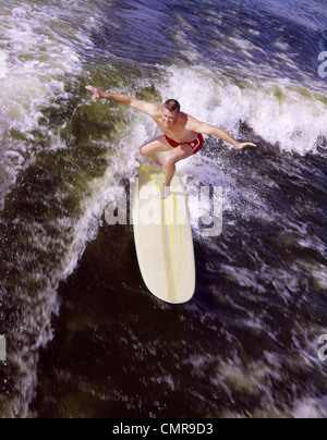 Anni Cinquanta anni sessanta GIOVANE UOMO RED COSTUME DA BAGNO GIALLO con la tavola da surf a cavallo di un WAVE SURF Foto Stock