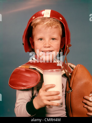 Negli anni sessanta il ragazzo biondo sorridente indossando il casco ROSSO FOOTBALL SPALLINA HOLDING bicchiere di latte e il calcio guardando la fotocamera Foto Stock