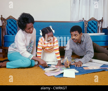 1960 anni sessanta retrò famiglia americana africana madre padre figlia SEDUTA SUL SOGGIORNO PIANO CON blueprint scaglie di vernice Foto Stock