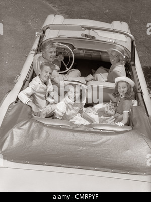 Anni sessanta ritratto di famiglia padre figlio di madre di due figlie in autovettura convertibile OUTDOOR cercando fino alla fotocamera Foto Stock