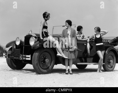 1920s 1930 QUATTRO DONNE INTORNO CABRIO TOURING CAR A SEASHORE due in costumi da bagno e due vestiti per la moda OUTDOOR Foto Stock