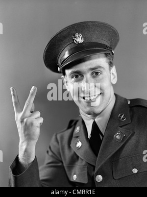 1940s RITRATTO DI GIOVANE UOMO DELL'ESERCITO IN UNIFORME sorridente e facendo segno di vittoria con la mano Foto Stock