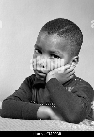 Negli anni quaranta anni cinquanta ritratto di triste infelice AFRICAN-AMERICAN BOY testa in appoggio sulla mano guardando la fotocamera Foto Stock