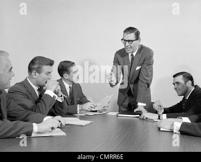 Anni sessanta 5 executive imprenditori riuniti a tavola per conferenze di un uomo in piedi Foto Stock