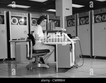 Negli anni sessanta la donna nel Mainframe Computer sala circondata da molti dati unità a nastro seduto alla scrivania digitando su una macchina da scrivere indoor Foto Stock