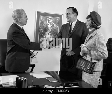 Anni sessanta giovane marito e moglie si stringono la mano con il prestito della Banca MANAGER BUSINESS INDOOR Foto Stock